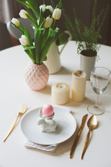 easter festive table details. Dining place decorated in pink and gold tones, with flowers, candles, bunny and eggs.