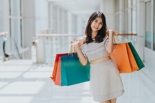 Happy Asian beautiful woman enjoying and smiling with colorful shopping bag in her both hand in mall.