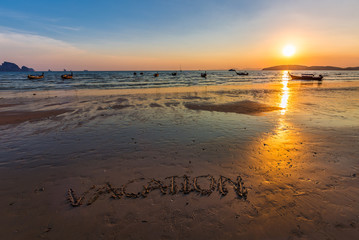 Vacation text written on the beach in Ao Nang, Krabi, Thailand at sunset.