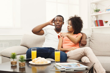 Obraz na płótnie Canvas Surprised african-american young couple watching TV at home