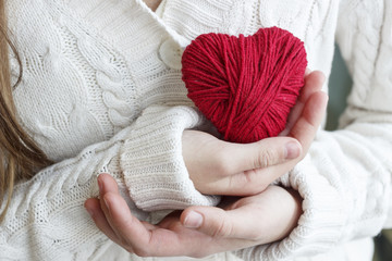 Children's hands hold a heart of red thread for knitting.