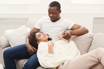 Obraz premium Smiling black couple having rest on sofa at home