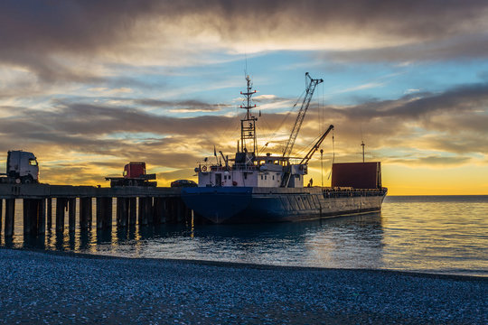 Small port, cargo ship and cranes on the sunset