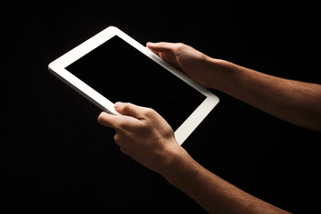 Man holding tablet with blank screen at black background