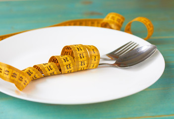 A white plate, a spoon with a fork and a measuring tape. The concept of healthy eating.