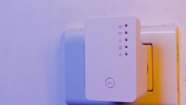 Man press with his finger on WPS button on WiFi repeater which is in electrical socket on the wall
