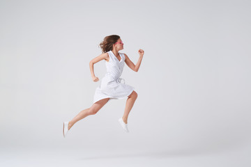 Fototapeta na wymiar Joyous girl in dress jumping up in air over background in studio