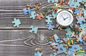 puzzles, alarm clock on the background of a wooden table. a game. time. pieces