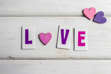 Colorful wooden hearts and letters making word love on white wooden background