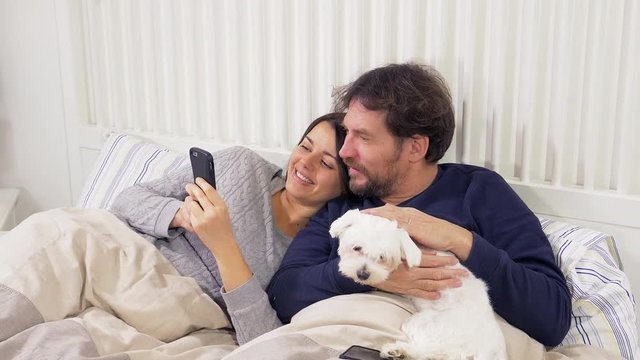 Happy couple in love looking pictures on phone holding dog
