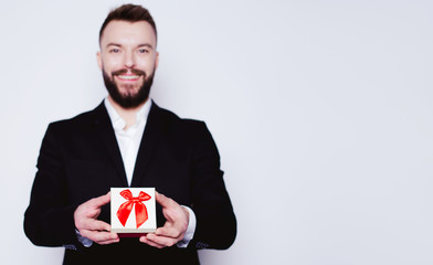 Handsome Smiling man in an elegant black suit with a gift box in hands looks at the camera on the white background isolated.