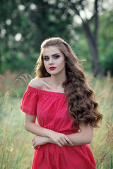Beautiful young caucasian girl with long wavy hair. Portrait of a woman in a red dress. Shooting outdoors, looking at the camera