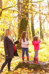 Pregnant mother enjoying with her two daughters in park on sunny autumn day.