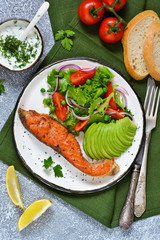 Food background. Baked trout with garnish of vegetable salad and avocado, with cream sauce on a concrete background.
