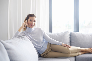 Attractive mature woman talking with somebody on mobile phone while sitting on couch at home