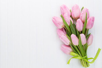 Fresh pink tulip flowers bouquet on shelf in front of wooden wall.