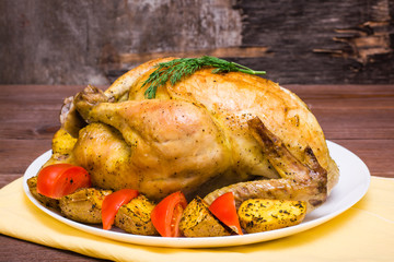 Baked whole chicken with a garnish of potatoes and tomatoes on a plate