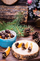 Ready-to-eat mandarins in chocolate with ground walnut on the trunk of a tree and in a bowl. Christmas decoration