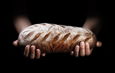 Une miche de pain fraîchement cuit dans les mains d& 39 un boulanger sur fond noir.