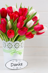 Fresh red tulip flowers bouquet on shelf in front of wooden wall.