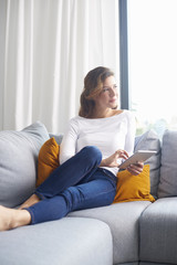 Woman browsing on the internet. Smiling middle aged woman using digital tablet while relaxing on sofa at home.