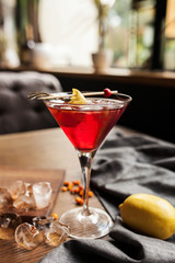 red alcoholic cocktail in a glass with ice and sea-buckthorn on a wooden table