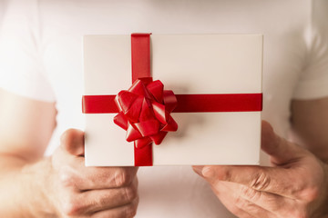 Man hands holding white gift box with red ribbon , close up. Valentines day concept