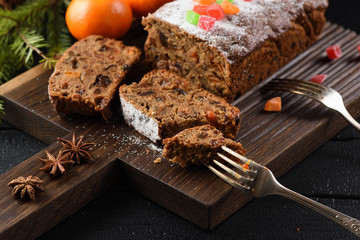 Slices of traditional English fruit cake with candied fruits served with clementines and star anise on oak board