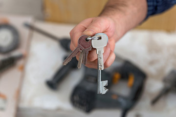Man's hand holding keys with a construction in background