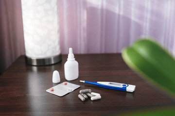 Electronic thermometer and tablets lie on a wooden bedside table.