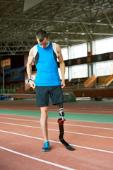Fototapeta premium Full length portrait of young amputee athlete standing on track before running practice in modern indoor stadium copy space