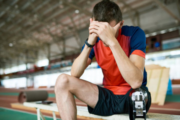 Portrait of young amputee athlete taking break from practice sitting on bench resting head on hands, copy space