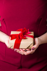 Present for Valentine`s day or birthday for a woman. Gift with red ribbon velour satin tied bow in female hands, red dress, light skin, copy space