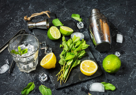 Mojito cocktail making. Mint, lime, glass, ice, ingredients and shaker on stone background