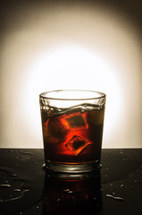 Glass of whiskey with ice / In the picture a glass with whiskey and three slices of ice, standing on a table filled with liquid