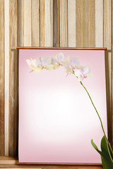 Poster with space for text with an orchid in the foreground and a wooden table and a wall in the background