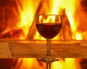 Glass of red wine against cozy fireplace background, winter vacation.