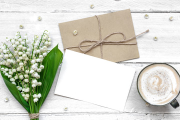 blank white greeting card and envelope with spring lily of the valley flowers and cup of cappuccino