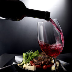 Closeup of red wine pouring into a glass with cheese and meat
