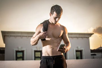 Handsome shirtless man using mobile phone after workout outdoors.