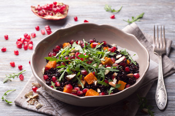 Salad with black rice, baked pumpkin, pomegranate seeds, arugula and nuts on a gray background. Delicious vegan food