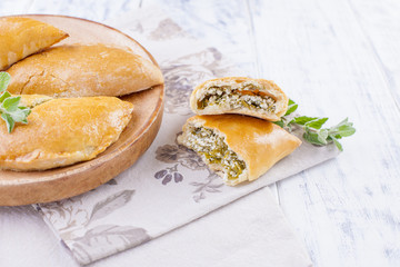 Fresh homemade pies with cheese and greens for breakfast. Portion pies. On a wooden plate and on a white background. Free space for text or advertising.