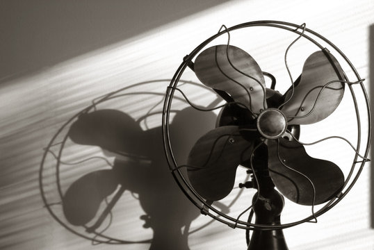 Antique Fan With Light Streaming Through The Window Blinds. A Film Noir Take On A Classic Antique Cooling Fan With Shadows And Light Projected Onto The Rear Wall.