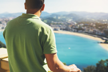 Fototapeta premium Hipster młody człowiek patrząc na taras widokowy podczas wakacji w San Sebastian, ciesząc się widokiem na morze na górze i oceanie, podróżnik turystyczny na tle panoramiczny widok na miasto