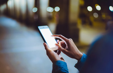 Woman pointing on blank screen smartphone on background bokeh light in night atmospheric city, hipster using in hands clean gadget mobile phone closeup, mockup street, online wifi internet concept