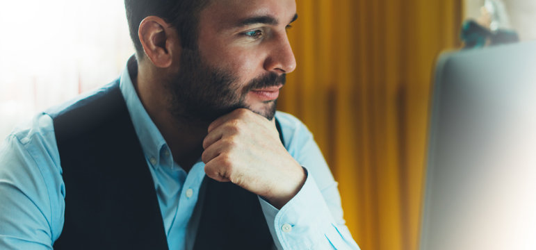 Bearded young businessman working on modern office at night. Consultant man thinking looking in monitor computer. Manager typing on keyboard in coworking workplace, startup project concept in studio