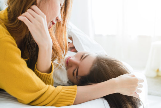 Beautiful young asian women LGBT lesbian happy couple hugging and smiling while lying together in bed under blanket at home. Funny women after wake up. LGBT lesbian couple together indoors concept.