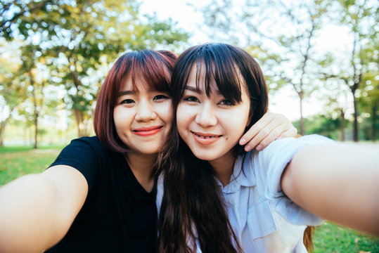 Two beautiful happy young asian women friends having fun together at park and taking a selfie. Happy hipster young asian girls smiling and looking at camera. Lifestyle and friendship concepts.