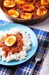 Traditional oriental dish - curry Golden eggs. Egg curry from Myanmar, India, Indonesia, Pakistan. Boiled, stewed, fried eggs with tomato vegetable sauce. Rice for lunch. Table is served for dinner.