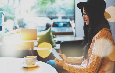 a young hipster girl reads news on a modern tablet. beautiful business woman plans meetings using the application on the pad while sitting in a cozy coffee shop. Bokeh light, film effects © JKstock